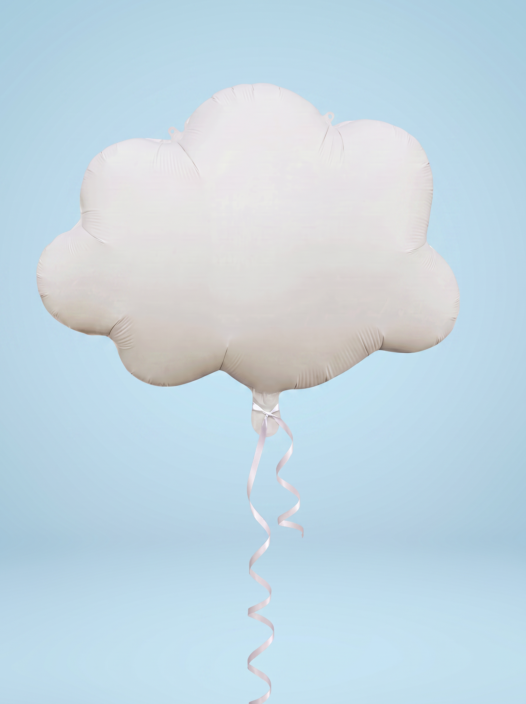 A cloud-shaped foil balloon in a very pale pink or blush tone, with a long matching pink ribbon trailing downward, shown against a soft light blue studio background.
